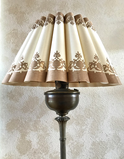 Classic floor lamp with pleated cream and brown patterned lampshade and brass base against textured wall.