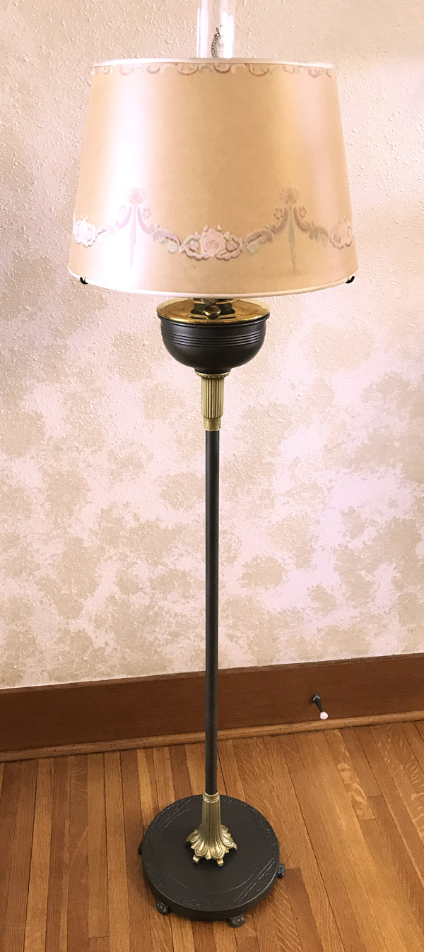 Tall vintage floor lamp with beige floral lampshade, black and gold stand on wooden floor.
