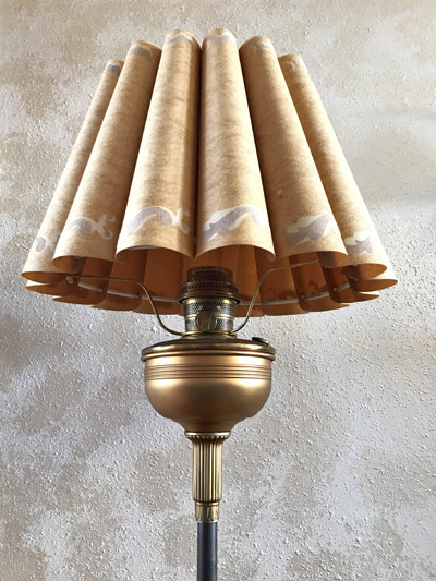 Vintage floor lamp with a beige pleated lampshade and brass base against a textured wall.