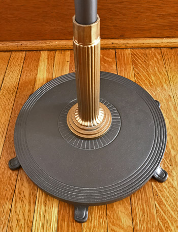 Black round base with ridges and gold ribbed pole on a wooden floor.