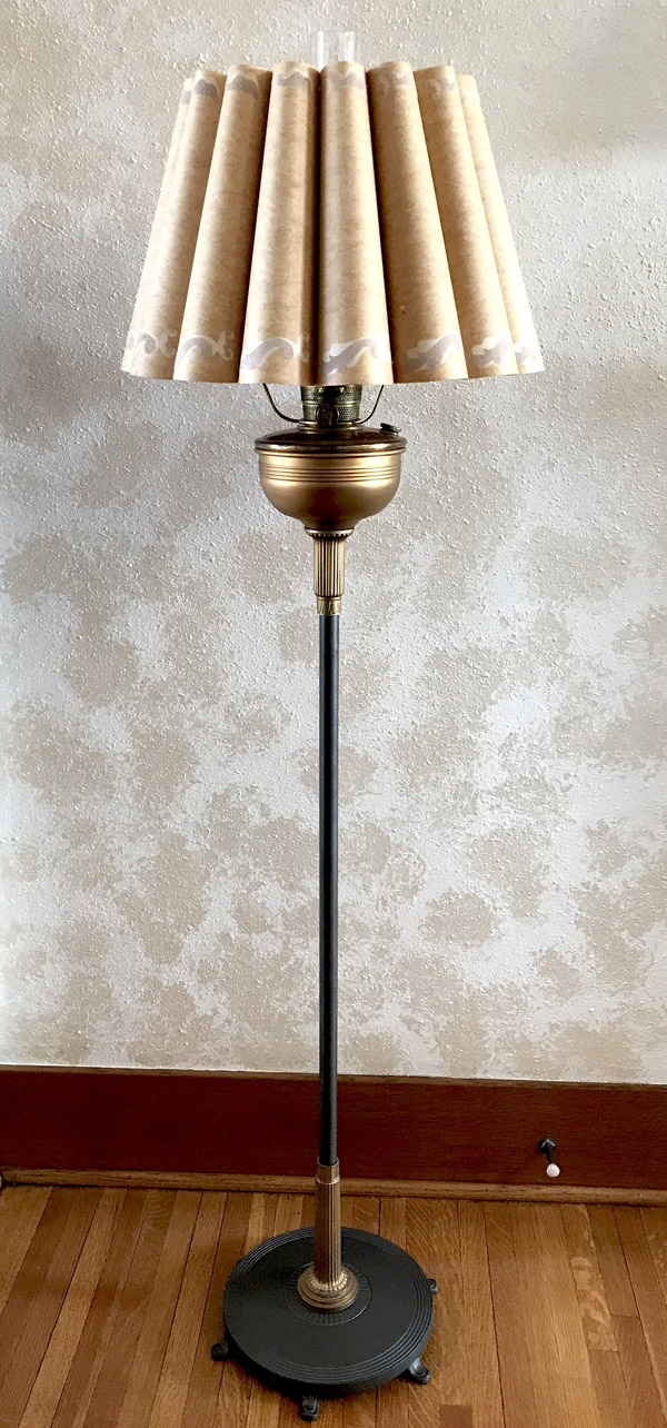 Vintage standing lamp with pleated beige lampshade against textured wall on wooden floor.