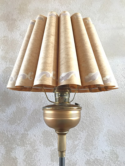 Vintage lamp with a pleated beige paper lampshade against a textured wall.