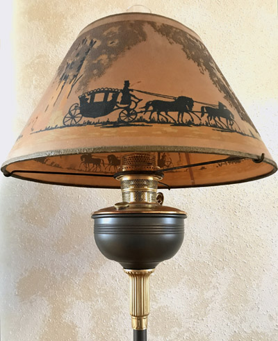Antique lamp with a painted lampshade depicting a horse-drawn carriage scene in black silhouette.