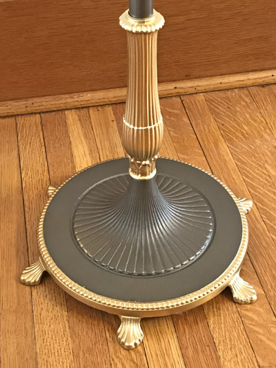 Ornate lamp base with gold accents on wood floor near wooden wall.