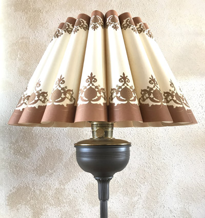 Vintage-style lamp with a pleated beige lampshade featuring brown decorative patterns on a dark metal base.