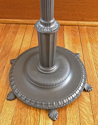 Close-up of a metallic lamp base with decorative ridges on a wooden floor.