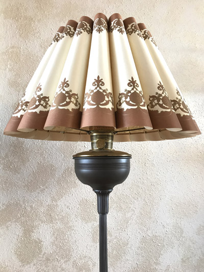 Floor lamp with pleated cream and brown decorative fabric shade against a textured wall.