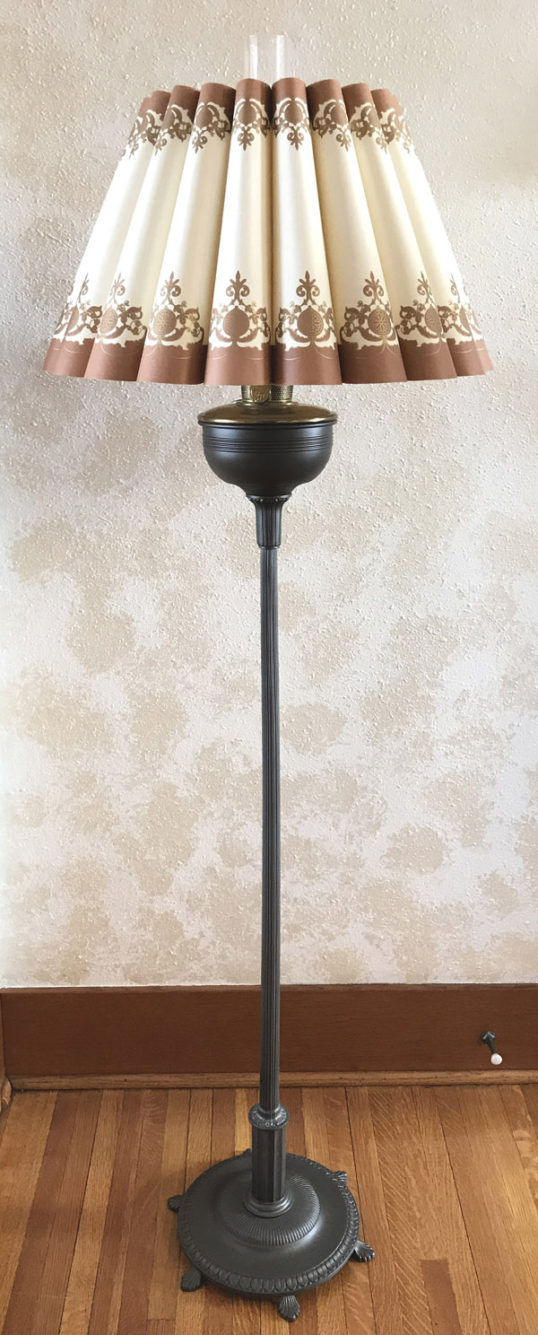 Tall vintage floor lamp with a pleated cream and brown patterned lampshade on wooden floor.