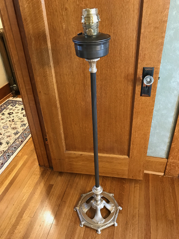 Tall vintage floor lamp with ornate gold base and black pole standing on hardwood floor.