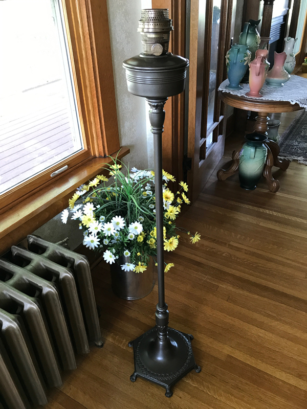Tall vintage metal floor lamp standing on hardwood floor next to a bucket of white and yellow flowers.