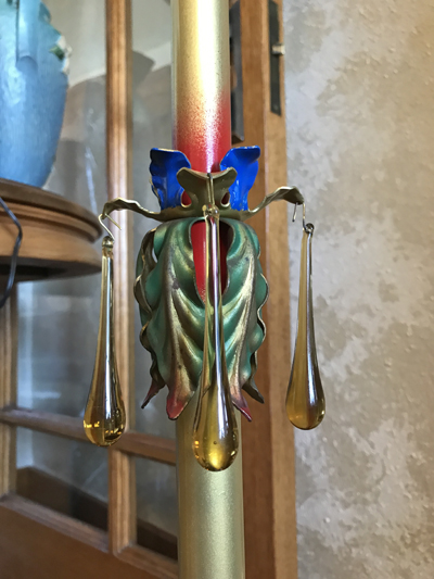 Decorative candleholder with three amber glass teardrops hanging from metal leaves on a tall candle.