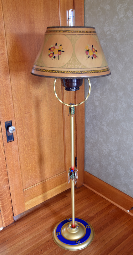 Tall vintage floor lamp with floral lampshade, gold pole, and blue-gold circular base on wooden floor.