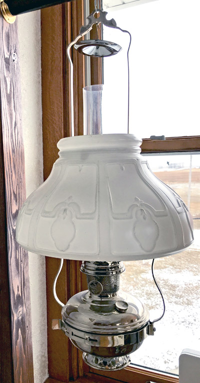 Vintage hanging oil lamp with frosted glass shade and metal base in front of a window.