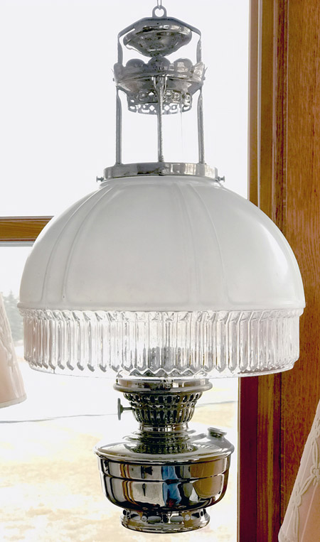 Vintage hanging oil lamp with white glass shade and ribbed glass trim near a wooden window frame.