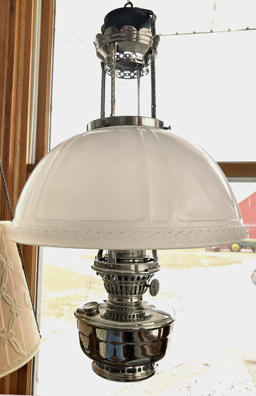 Vintage hanging oil lamp with a frosted glass shade near a window in daylight.