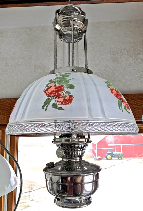 Hanging vintage-style lamp with white floral glass shade and ornate metal base near window.