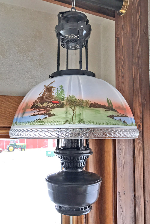 Vintage hanging lamp with painted countryside scene and ornate glass shade.