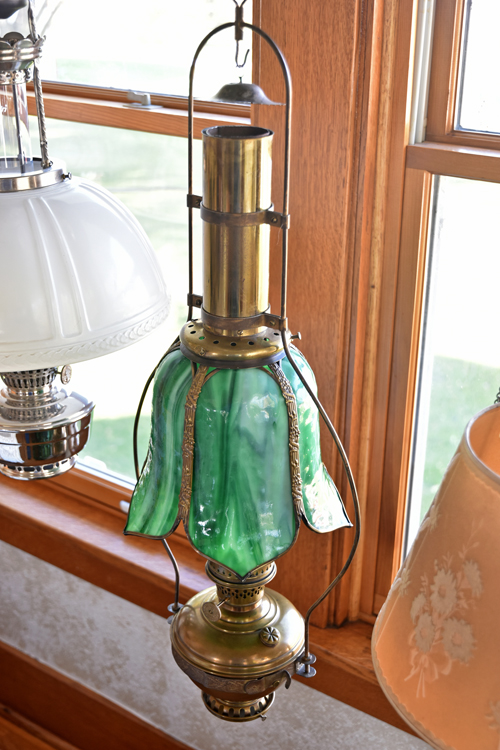 Antique hanging oil lamp with green glass shade and brass fittings near a window.
