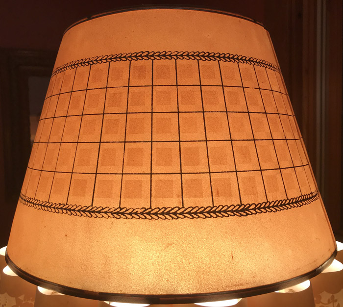 Tapered lampshade with a grid and wreath pattern glowing warmly from inside.