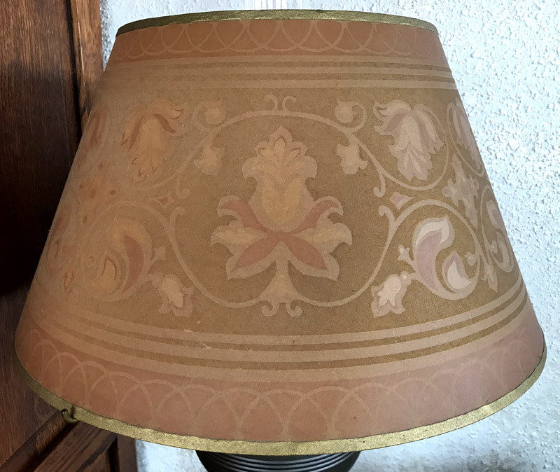Lamp shade with gold trim and a floral pattern in muted pink and beige tones.