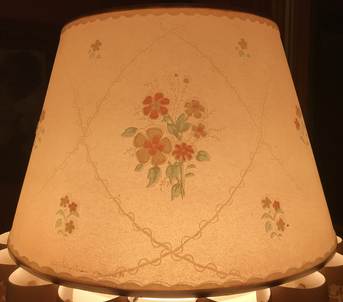 Illuminated beige lampshade with floral embroidery in orange, green, and beige colors.