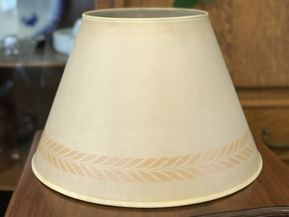 Beige lampshade with a subtle leaf pattern near the bottom edge on a wooden surface.
