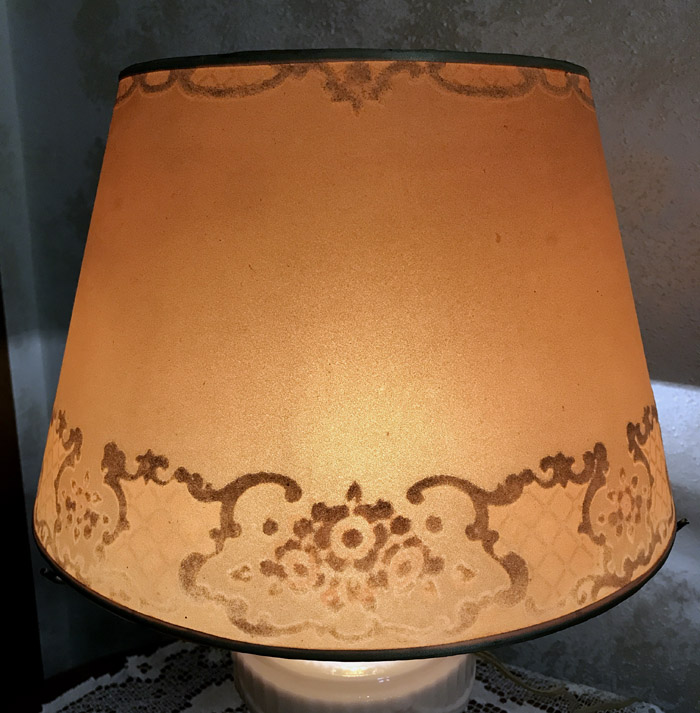 Lit vintage lampshade with ornate brown decorative patterns on a beige background.