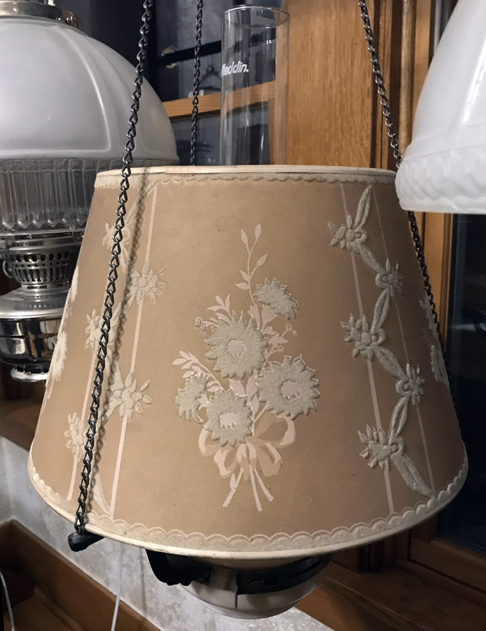 Beige fabric lampshade with embroidered floral patterns hanging by metal chains.