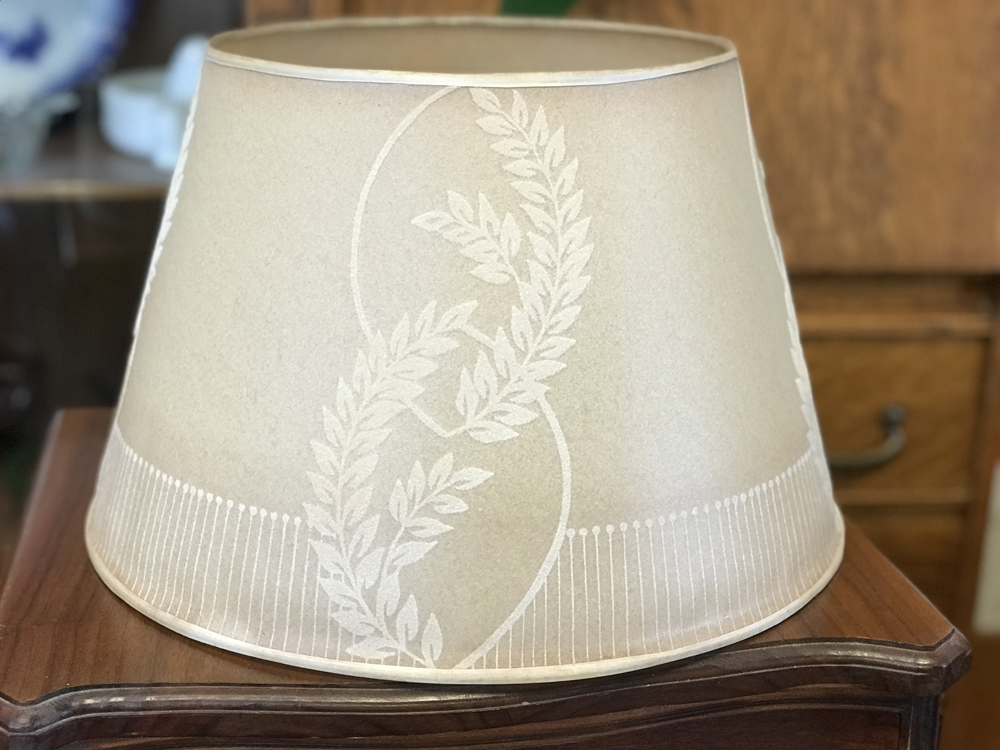 Beige lamp shade with white leaf patterns placed on a wooden table.