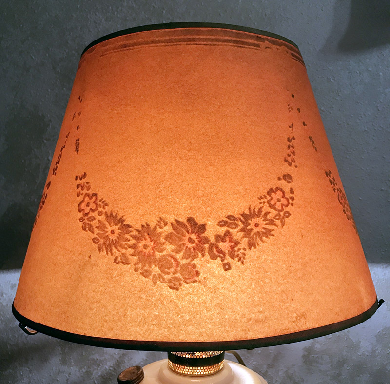 Lit vintage lampshade with a floral pattern casting a warm orange glow.