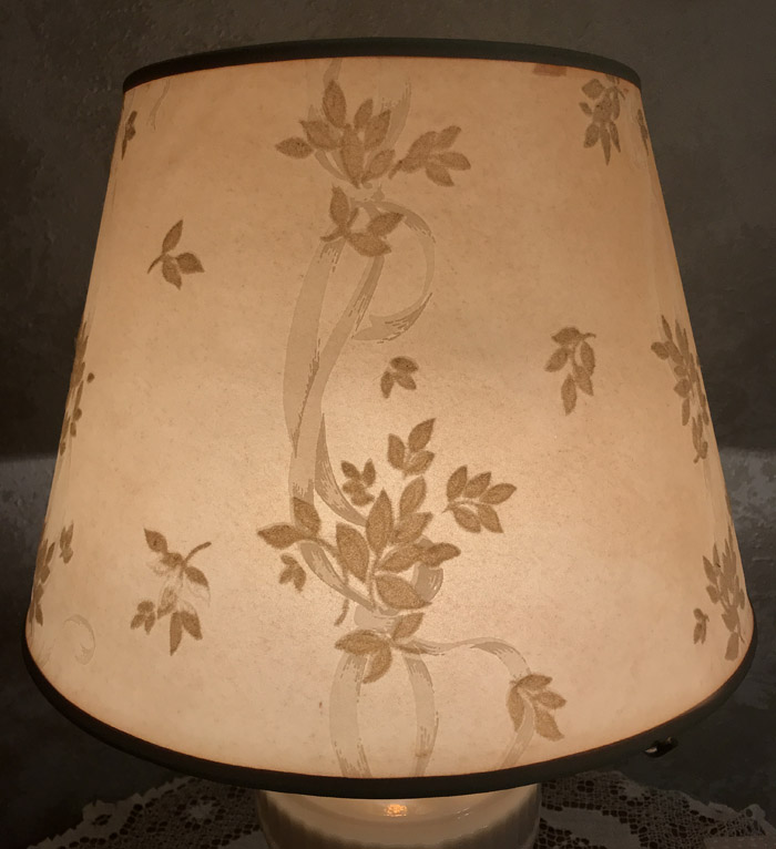 Beige lampshade with brown leaf and vine patterns lit on a lamp base.