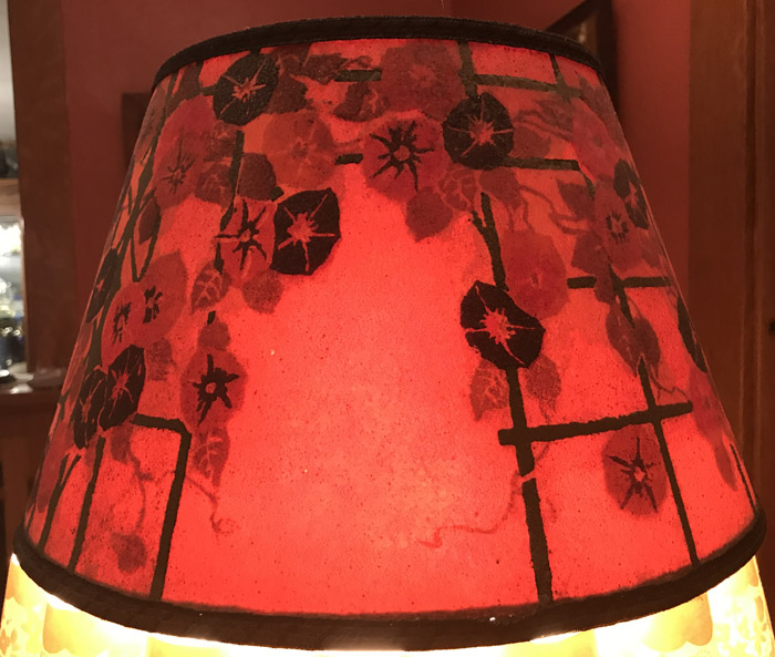 Red lampshade with a floral and geometric vine pattern in black on a warm background.