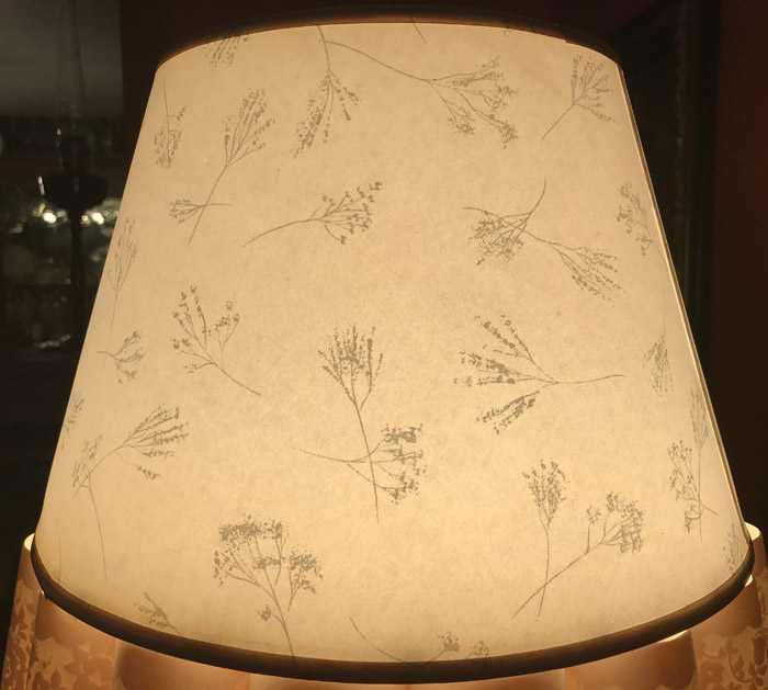 Close-up of a lamp shade with delicate floral branch patterns illuminated softly.