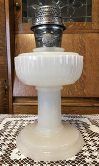 White vintage glass oil lamp with metal burner and wick holder on lace cloth.