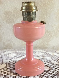 Vintage pink glass oil lamp with brass burner sitting on lace fabric.