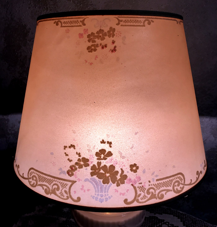 Lit beige lampshade with brown and pink floral and decorative patterns on it.