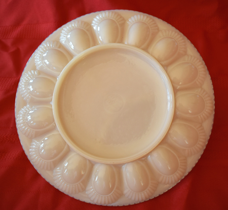 White ceramic deviled egg platter with 12 rounded molds on a red cloth background.