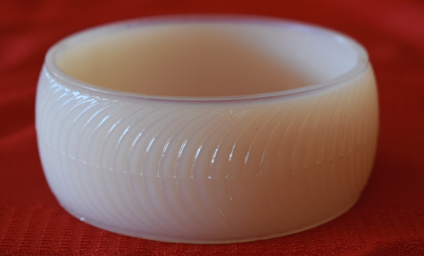 Smooth white bangle bracelet with textured curved lines on a red fabric background.