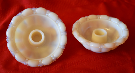 Two white ceramic candle holders with scalloped edges on a red fabric background.