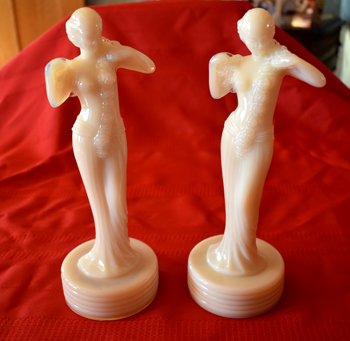 Two ivory-colored, female figurines standing on round bases on a red cloth background.