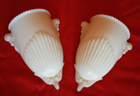 Pair of white vintage glass wall pockets with ornate details on a red background.