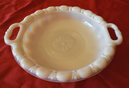 White decorative ceramic bowl with handles and embossed flower design on red fabric.