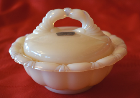 White vintage powder dish with ornate lid handle on red fabric background.