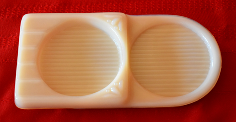 Cream-colored ceramic ashtray with two round indentations on a red fabric background.