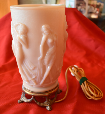 Pink art deco glass lamp with raised female figures on a decorative metal base with cord.