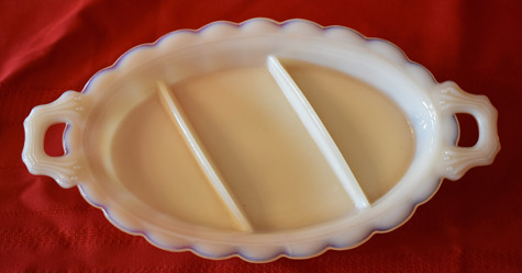 White divided serving dish with handles on each side on a red cloth background.