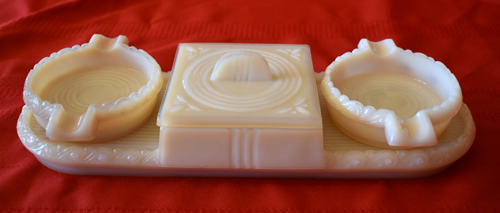 Cream-colored vintage cigarette tray with two ashtrays on a red cloth background.