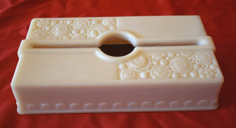 White rectangular tissue box cover with floral patterns on top and sides on a red fabric.