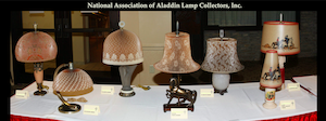 Table display of vintage Aladdin lamps with various shades at a collector's exhibition.