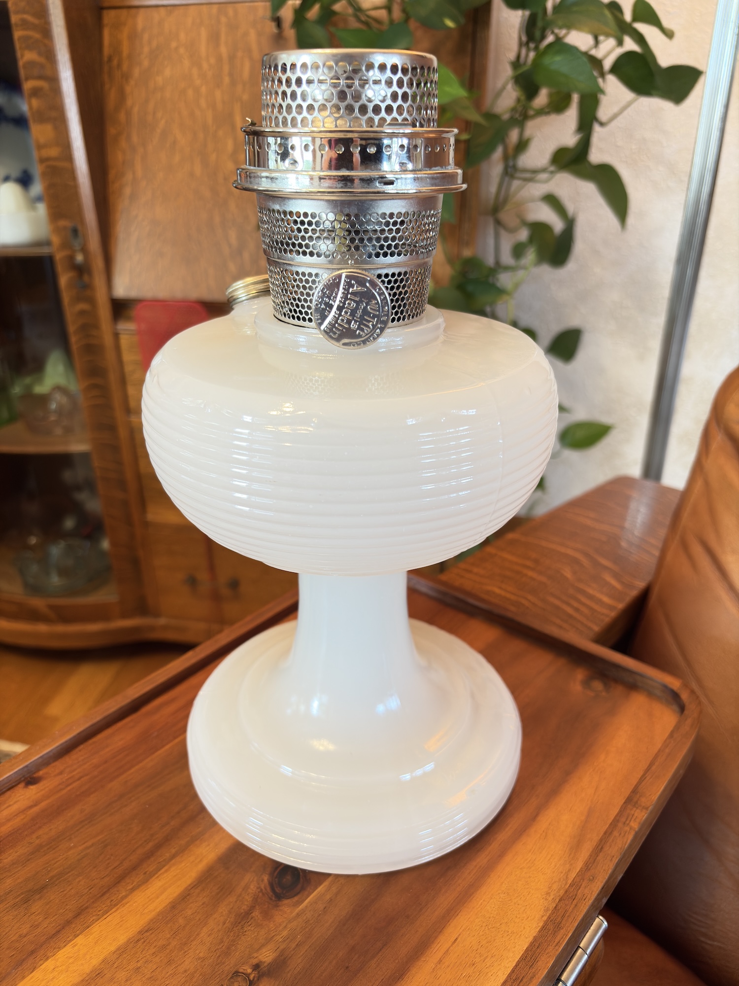 White glass vintage oil lamp with silver metal burner sitting on a wooden tray table.